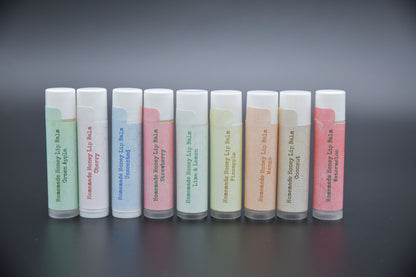 Nine honey lip balm tubes in assorted flavors arranged on a dark background