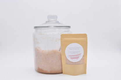 Peach-colored botanical bath salts in a pouch beside a large glass jar