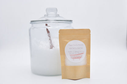 Pale blue botanical bath salts in a pouch beside a large glass jar