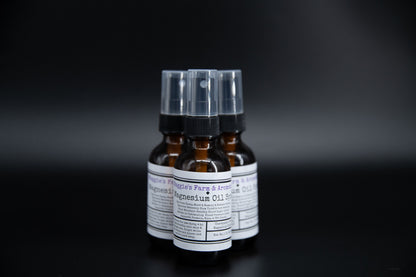 Three amber magnesium oil spray bottles on a dark surface