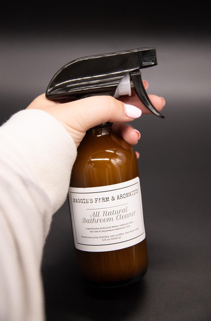 Hand holding a brown glass bathroom cleaner spray bottle